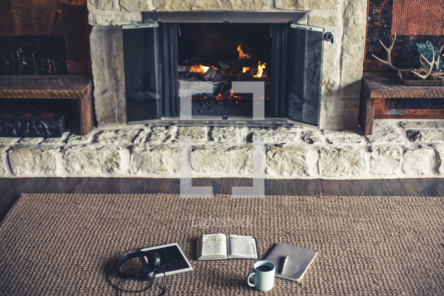 headphones, tablet, open Bible, pen, journal, and coffee cup by a fireplace 