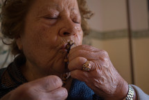 an elderly woman kissing a rosary 