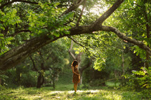 A pregnant woman standing in sunlight in a forest.