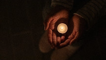 a votive candle in cupped hands 