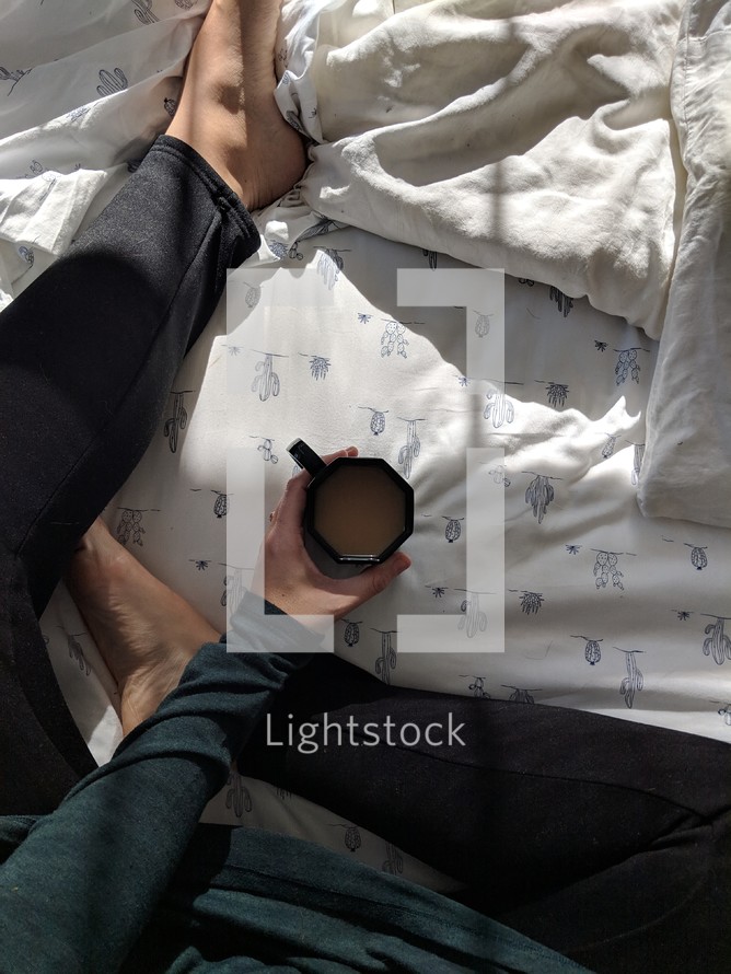 a woman sitting on a bed with a cup of coffee 
