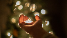 votive candle in a hand in front of a Christmas tree 