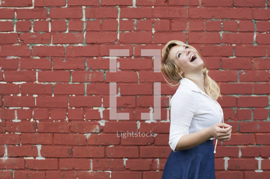 joyful teenage girl laughing in front of a red brick wall.
