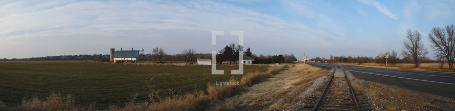 Panorama of a small town farm in Kansas. Field, barn, railroad tracks and a blue sky. 