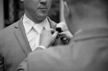 A groomsman pins a boutonniere to a groom's lapel.