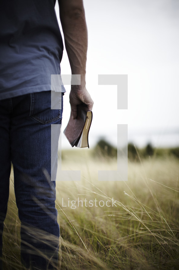 Young man standing in a field with Bible at his side