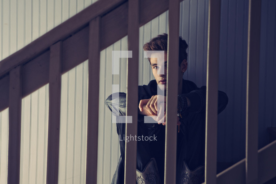 man sitting on stairs looking through rails