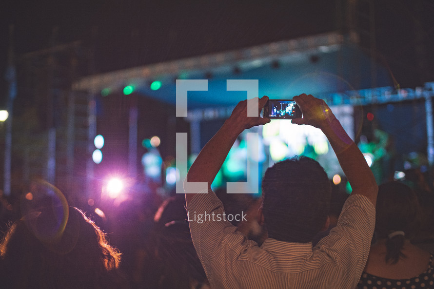 a man taking a picture of a stage with his cellphone at a concert 