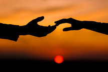 Valentine day. Silhouette of hands of woman and man reaching each other, touching fingers with tenderness on orange sunset sky background. Helping hands, save and support people concept. Friendship