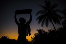 silhouette of a woman holding up a skateboard at sunset 