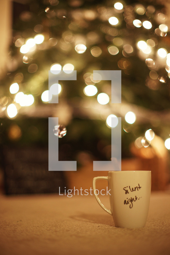 A mug with the words 'Silent Night' written on it - Christmas tree in the background