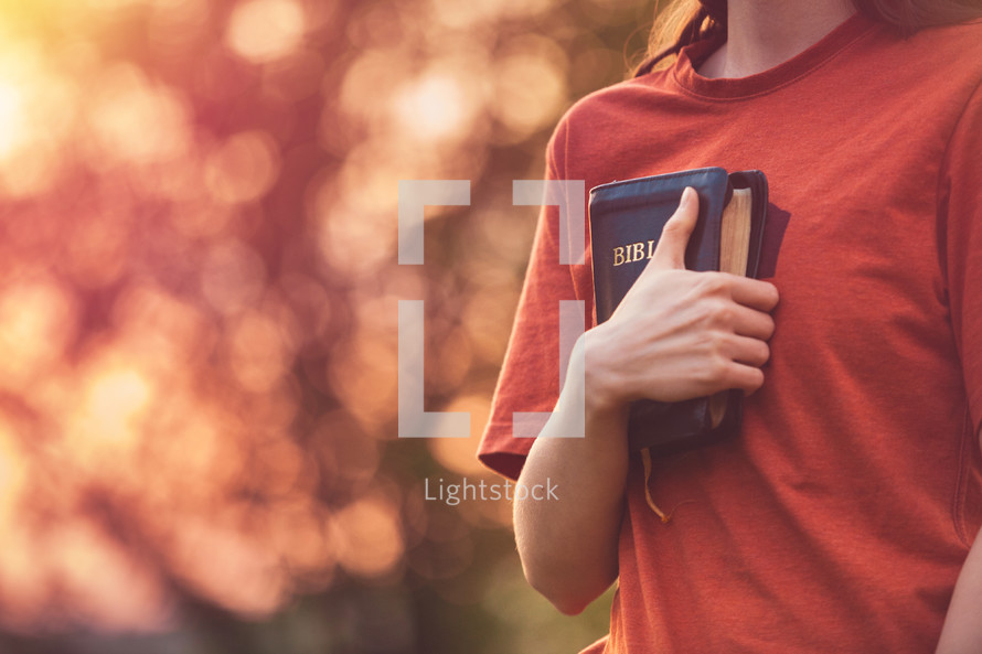 Girl holding a Bible tight as it is the only hope, beautiful warm color palette