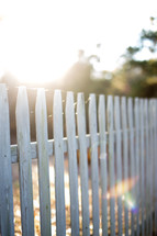 Sun shining through a white picket fence.