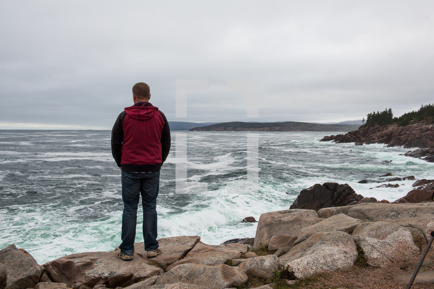 a man standing on a rocky shore looking out into the ocean 