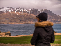 a woman looking out at snow capped mountains across a river 