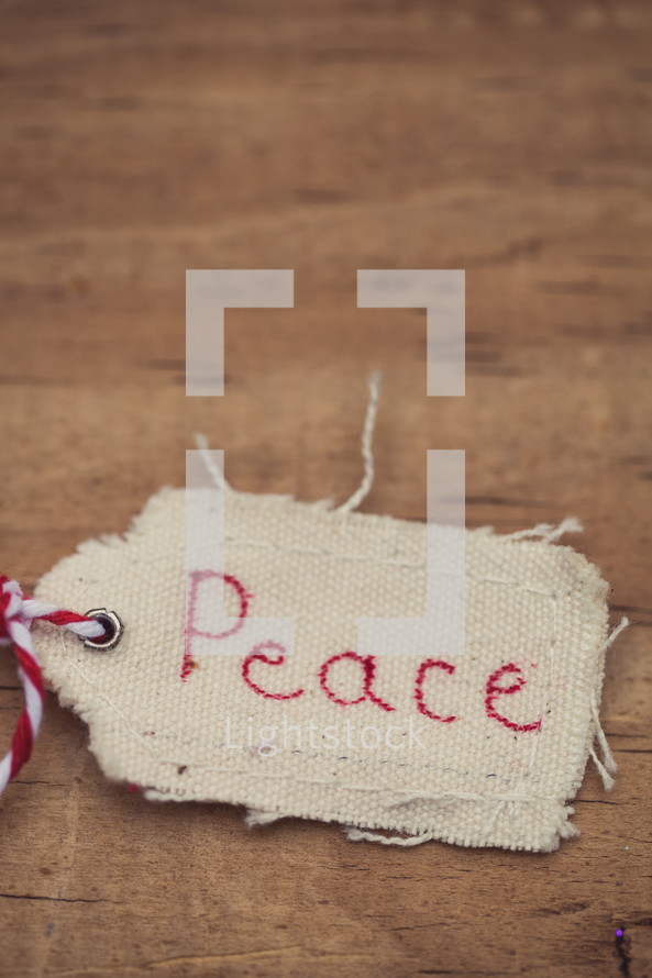 A fabric Christmas gift tag, labeled "Peace," on a wood grain background.