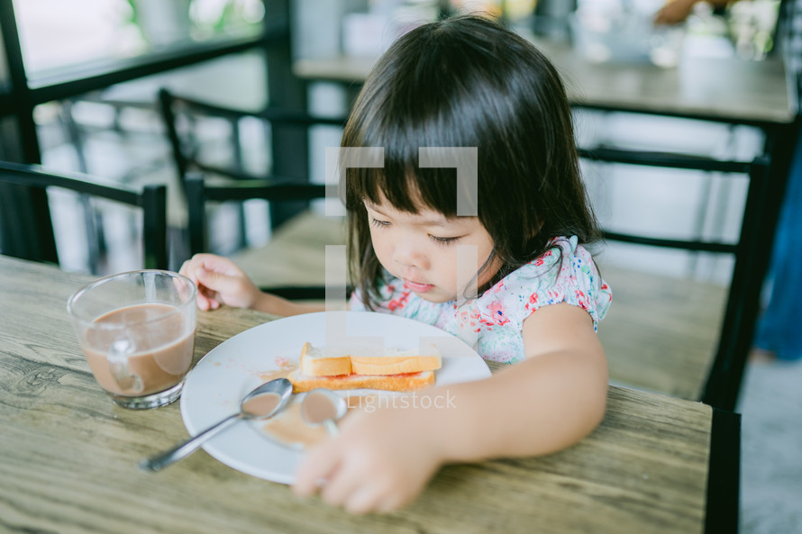 a toddler girl eating and playing with her food at a restaurant 