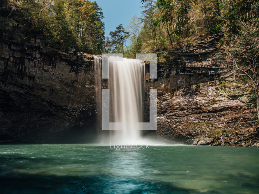 waterfall flowing over a cliff into a swimming hole 