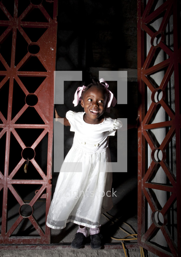 Smiling girl in white dress emerging from doorway.