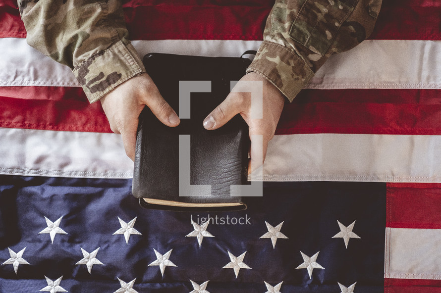 military man in uniform holding a Bible over an American flag 