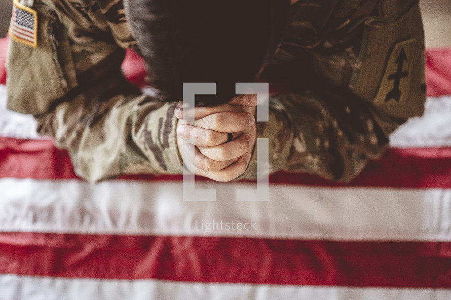 serviceman with head bowed praying over and American flag 