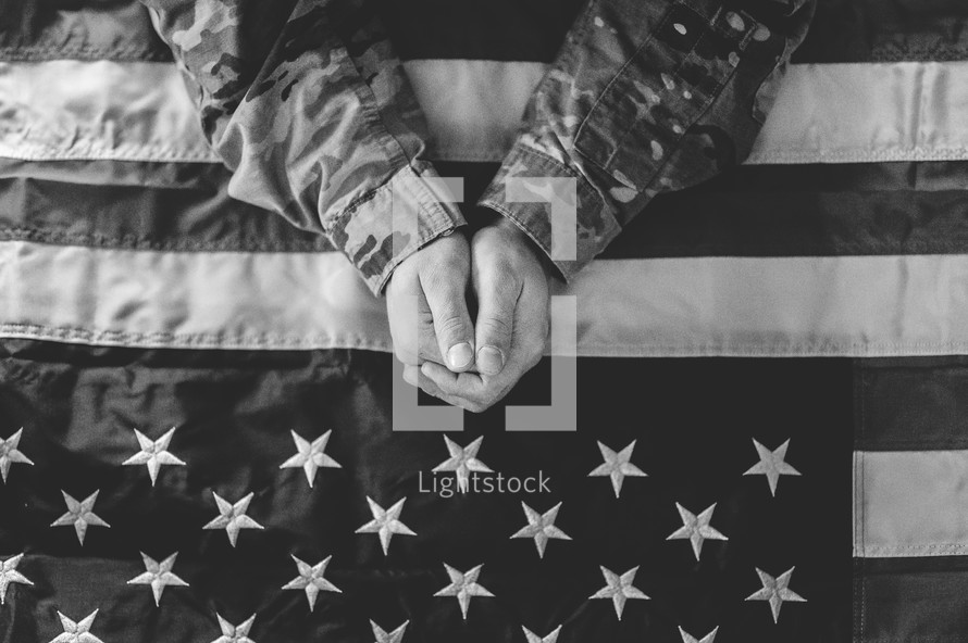 serviceman in uniform praying over an American flag 