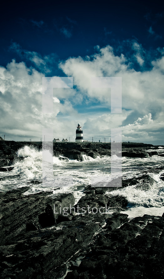 waves crashing into a rock wall near a lighthouse 