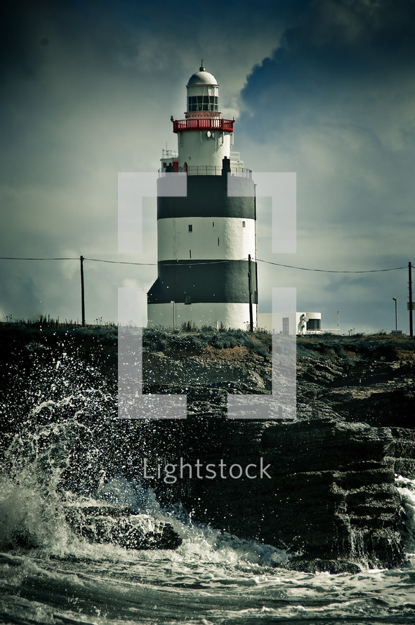 waves crashing into to a wall near a lighthouse