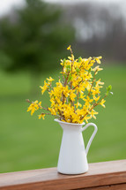 yellow flowers in a pitcher on wood railing 