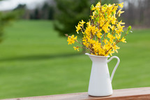 yellow flowers in a pitcher on a wood railing 