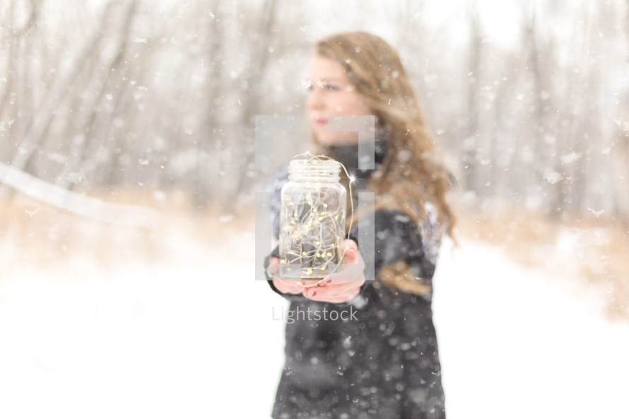 Girl in the snow with a jar of twinkle lights