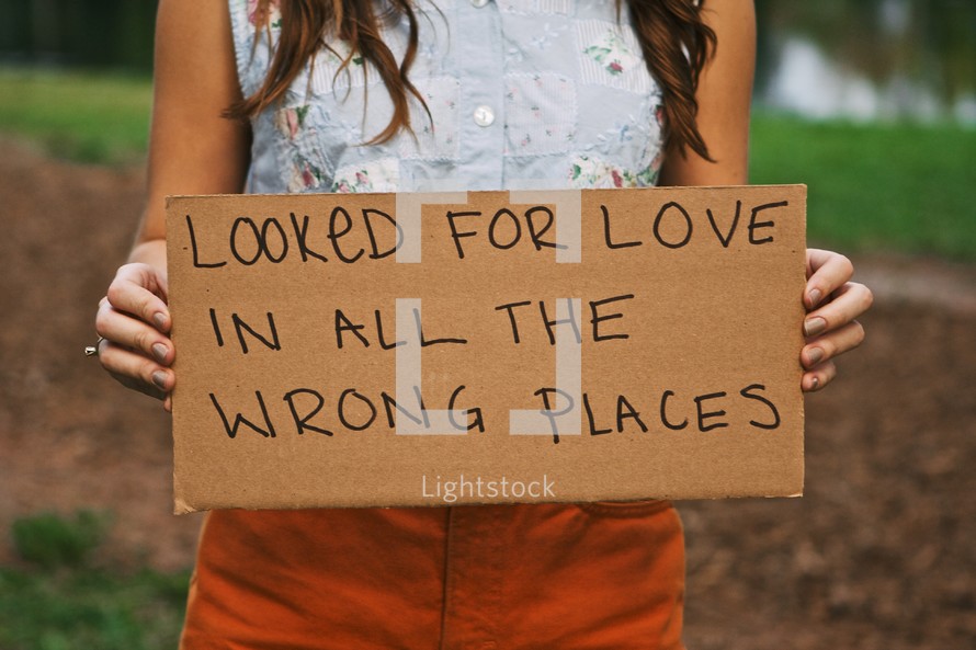 woman holding a sign with the words LOOKED FOR LOVE IN ALL THE WRONG PLACES
