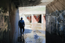 a man standing in concrete tunnels covered with graffiti 