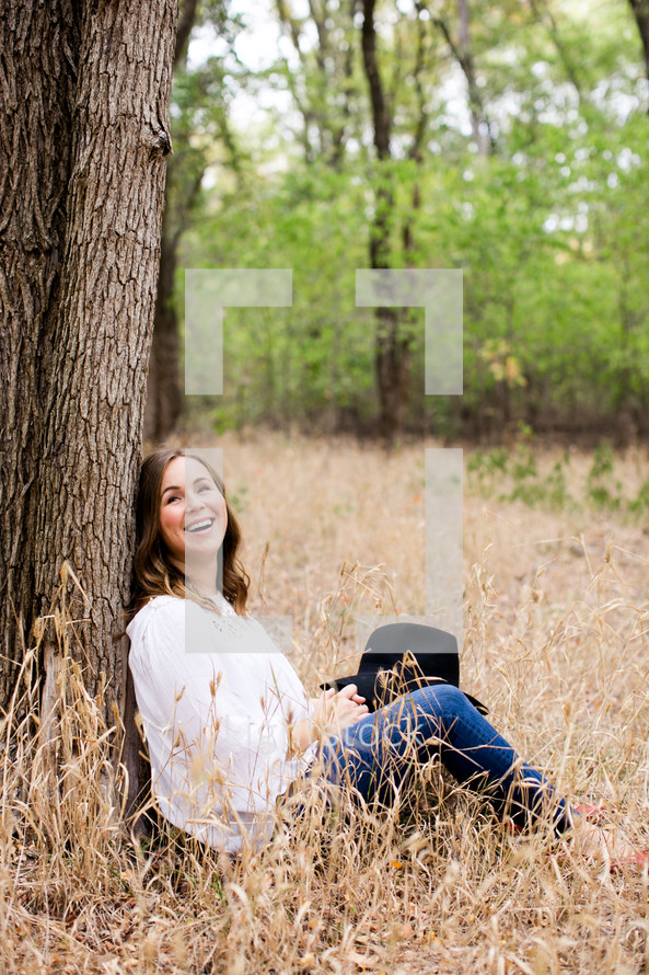 woman sitting leaning against a tree outdoors 