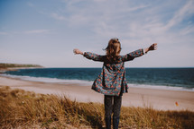 a girl standing on a shore with outstretched arms 