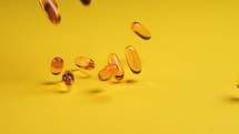 Pills or vitamins falling on yellow background