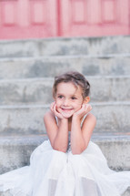 a little girl in a gown sitting on steps 