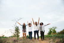 women with raised arms standing outdoors rejoicing 