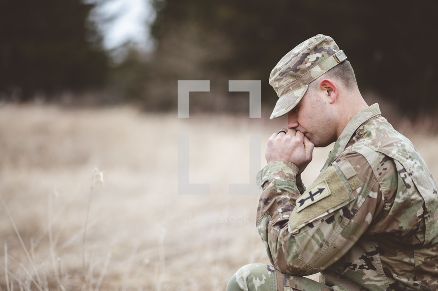 serviceman kneeling in prayer in a field 