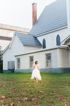 a girl in a dress walking through fall leaves in front of a church 