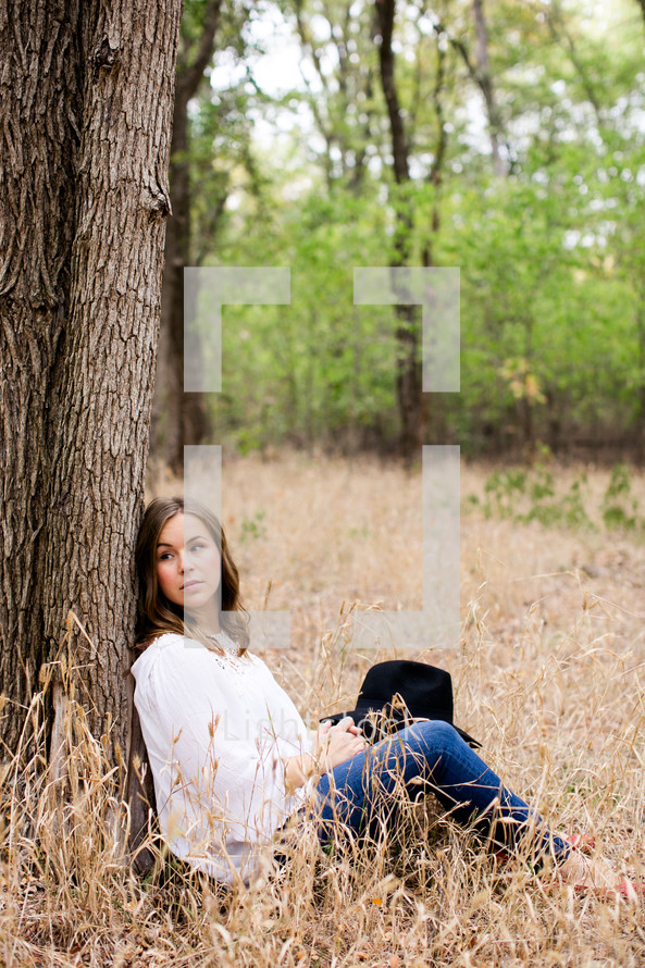 sitting, leaning against a tree, tree, outdoors, woman