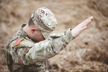 soldier with hand raised kneeling in a field 