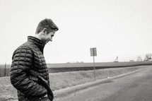 a man in a coat standing on the side of a road 