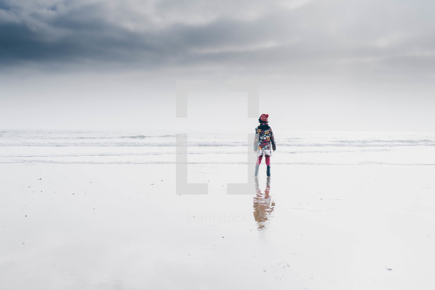 a girl in a winter coat and beanie standing on a beach in winter 