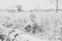 a toddler boy sitting in tall grass under bright sunlight 
