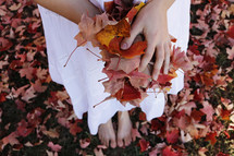 barefoot woman holding fall leaves 