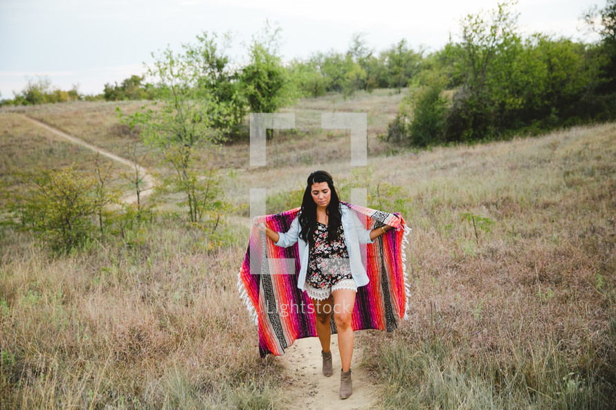 Woman walking up a hill wrapped in a blanket 