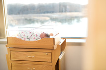 An infant swaddled and laying on a changing table.