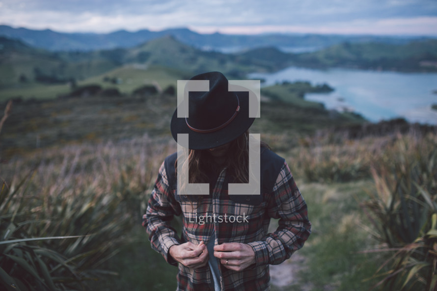 a man in a hat and plaid shirt standing on a mountain top 
