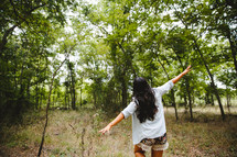 woman with open arms walking in a forest 